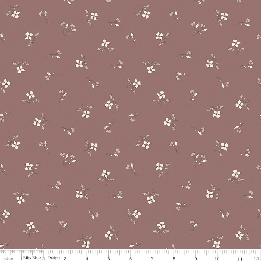 A close-up of a dusty mauve fabric with a repeating pattern of small white flowers and green leaves, with a ruler at the bottom indicating scale.