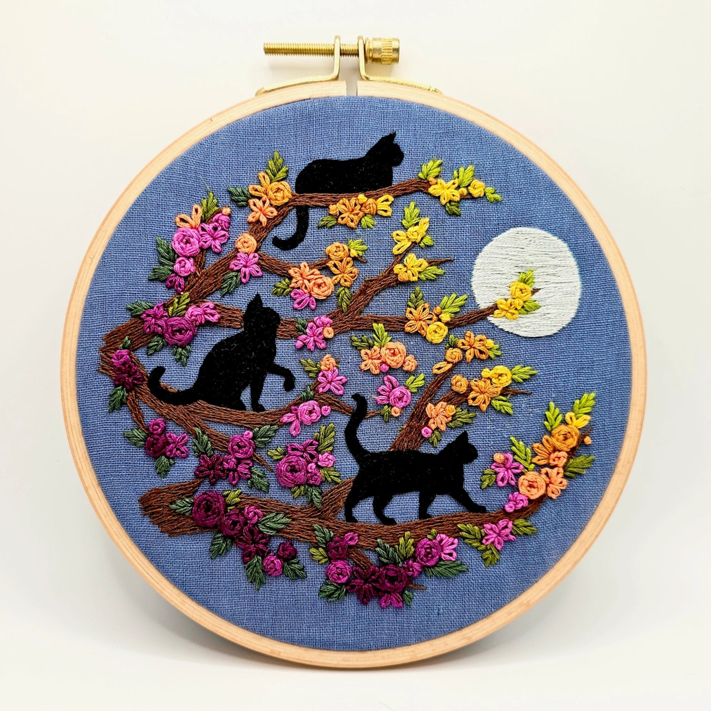 Embroidery hoop with black cats and flowers on a blue background
