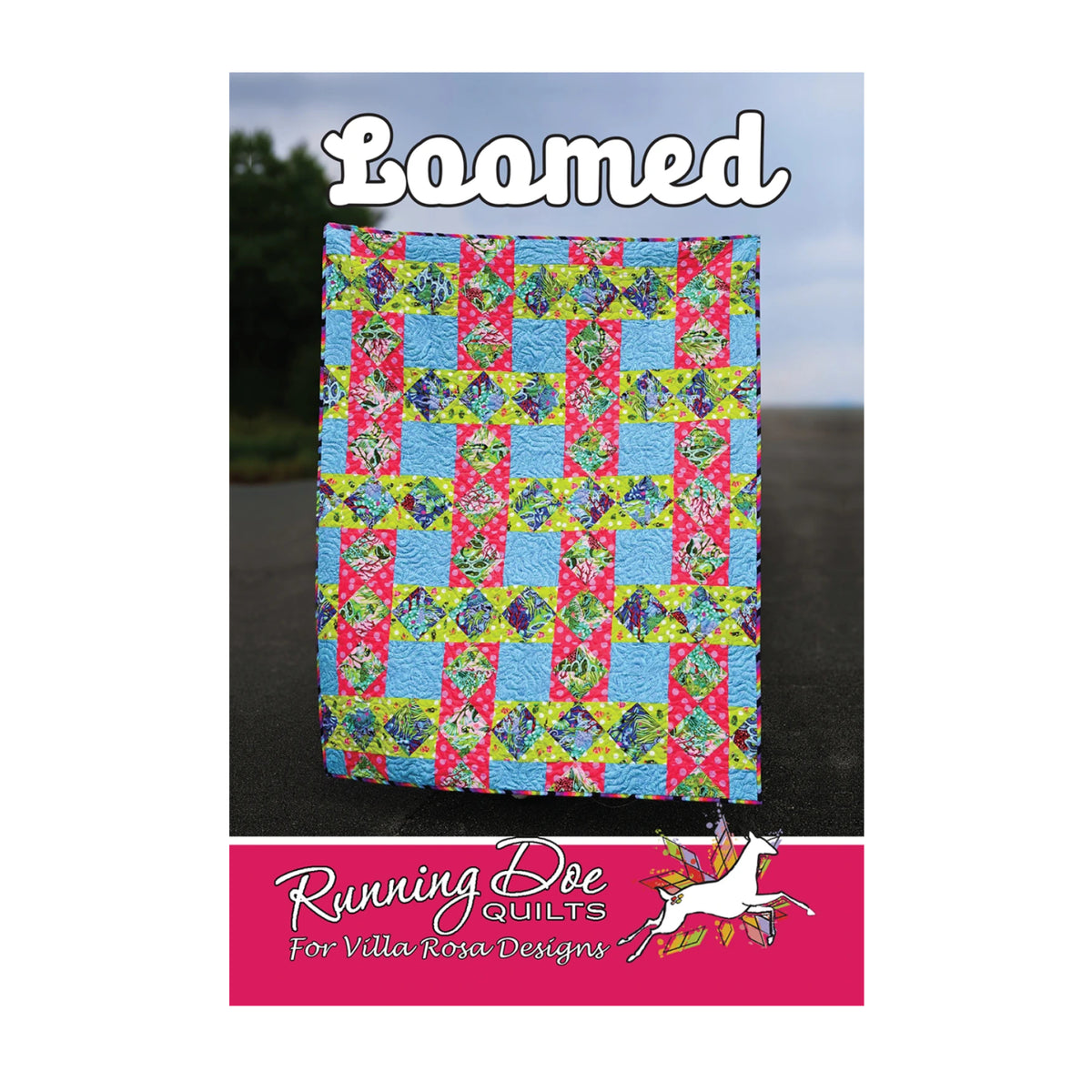 A quilted fabric square with a colorful patchwork design of blue, pink, and green floral checks, displayed outdoors on a dark surface with a blurred sky background. The image includes the text 'Boomed' at the top and a pink banner at the bottom reading 'Running Bee Quilts for Villa Rosa Designs' with a white bee illustration.
