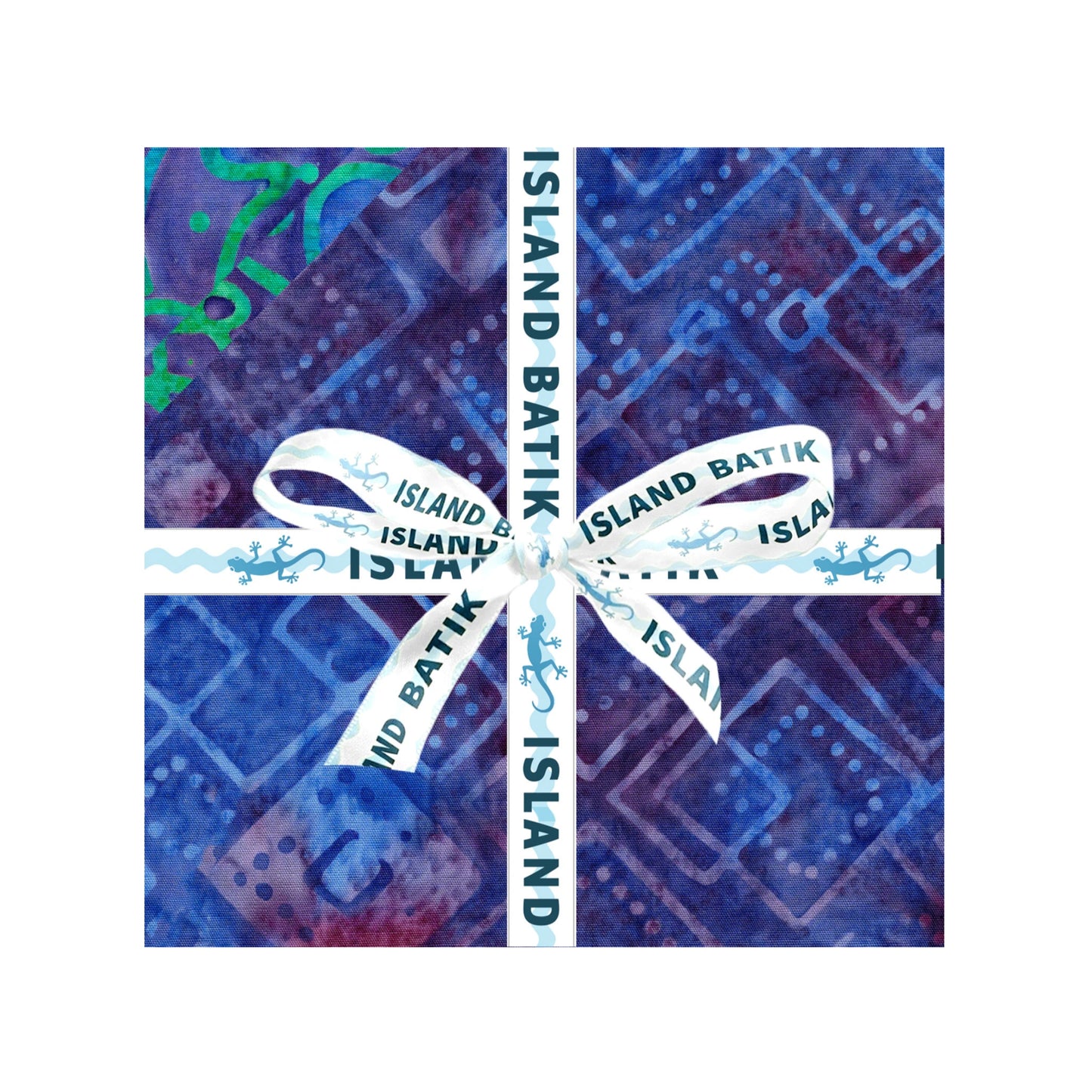 A square fabric bundle in blue and purple batik-patterned paper, tied with a white ribbon printed with 'ISLAND BATIK' and small lizard motifs, centered on a white background
