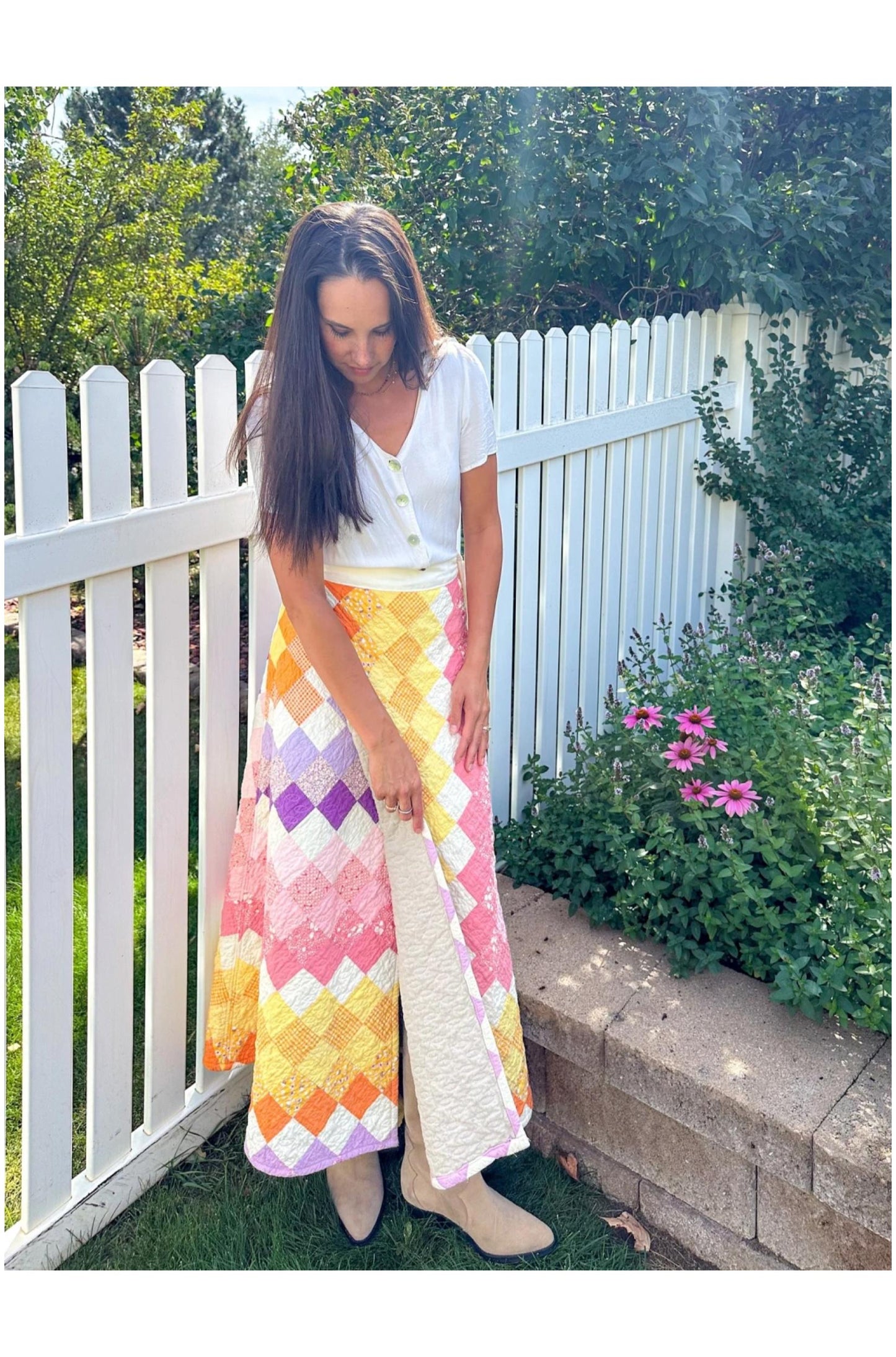 Woman wearing a colorful patterned skirt and white top in a garden setting.