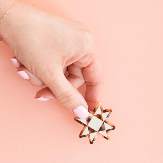Hand holding a geometric star-shaped object against a pink background