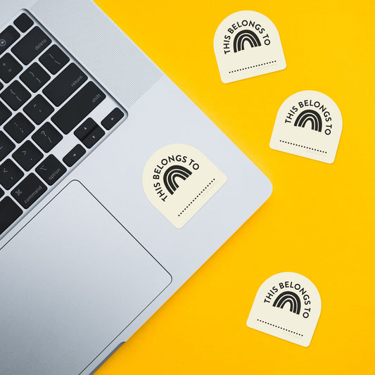 Four 'This Belongs To' stickers on a yellow background with a laptop.