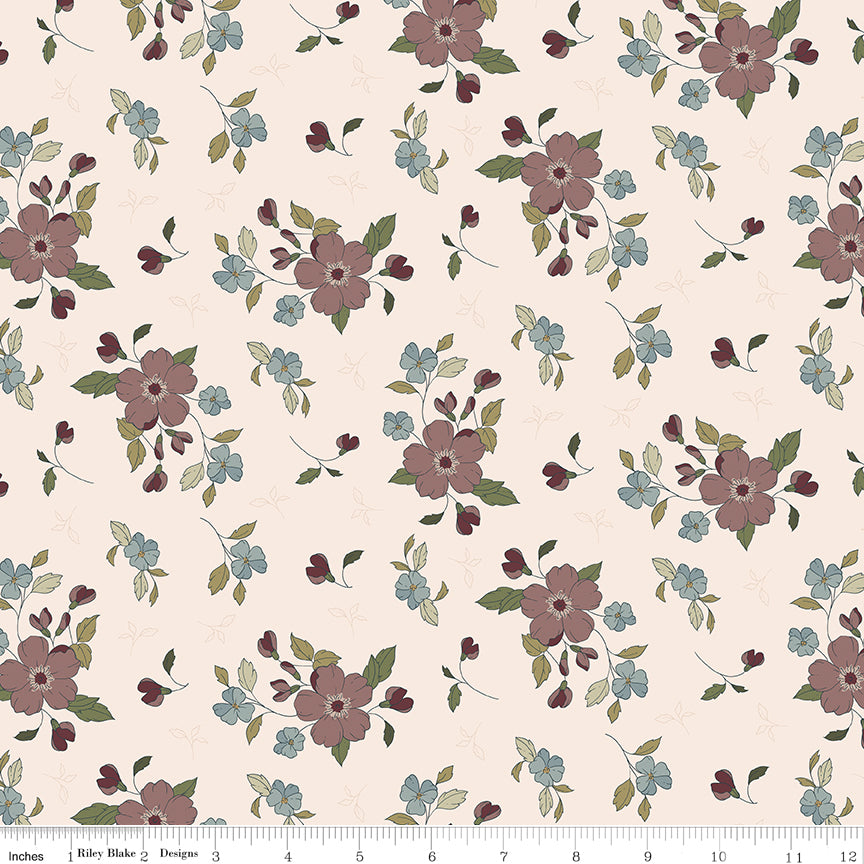 A repeating floral pattern on fabric with large dusty mauve-pink flowers, smaller light blue blossoms, muted green leaves, and small burgundy buds on a warm cream background. A ruler along the bottom edge shows the scale of the print.
