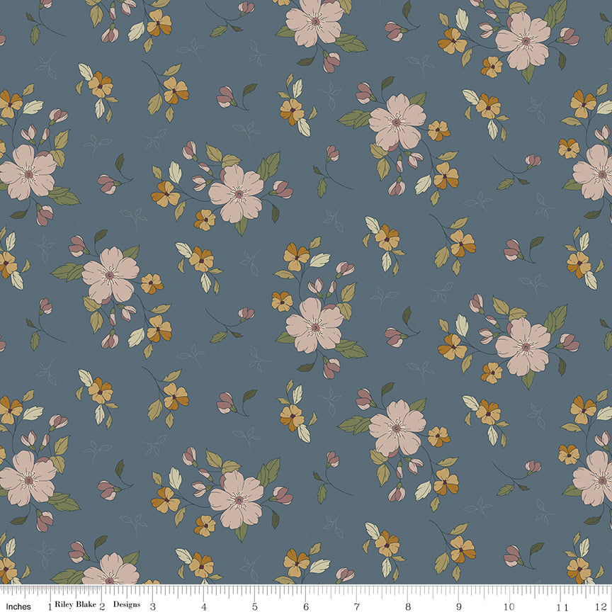 A repeating floral pattern on a muted blue-gray background, featuring pale pink blossoms, small yellow flowers, and green leaves. A ruler along the bottom edge shows scale and includes the text 'Riley Blake Designs'.