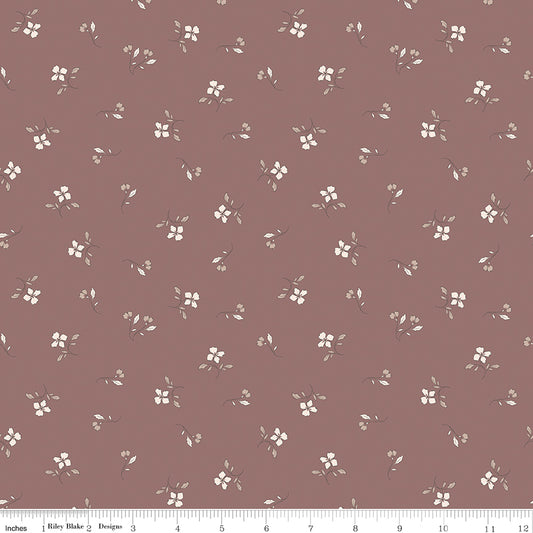 A close-up of a dusty mauve fabric with a repeating pattern of small white flowers and green leaves, with a ruler at the bottom indicating scale.