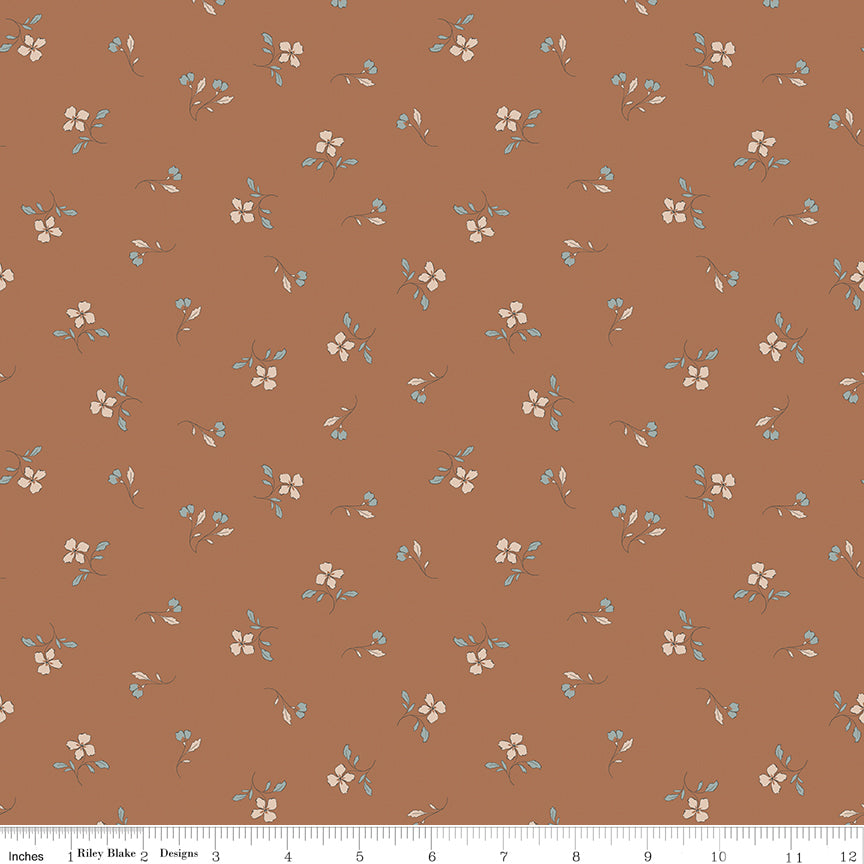 A repeating fabric pattern on a warm terracotta brown background, featuring small cream flowers with light blue leaves and stems. A white ruler along the bottom edge shows scale with the text 'Riley Blake Designs'.