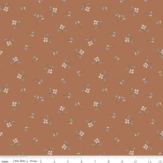 A repeating fabric pattern on a warm terracotta brown background, featuring small cream flowers with light blue leaves and stems. A white ruler along the bottom edge shows scale with the text 'Riley Blake Designs'.