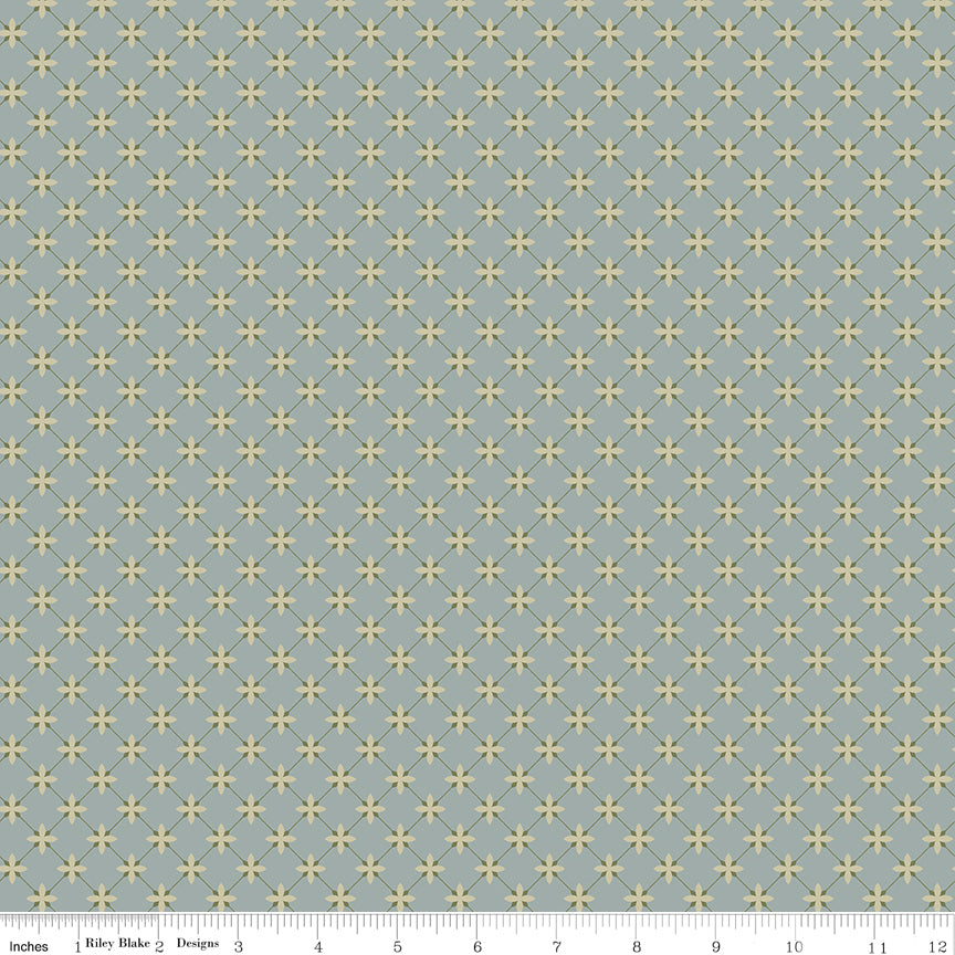 A repeating geometric pattern of small yellow four-point stars on a muted blue-gray background, shown as a fabric or wallpaper swatch with a ruler along the bottom edge.
