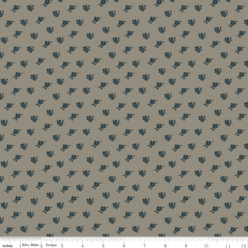 A repeating fabric pattern of small dark blue floral motifs on a warm taupe-beige background, with a ruler along the bottom edge showing scale.
