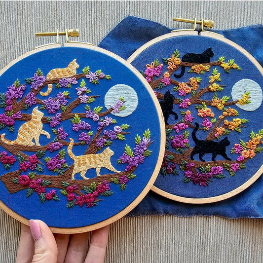 Two embroidery hoops with cat-themed designs on a blue fabric background.