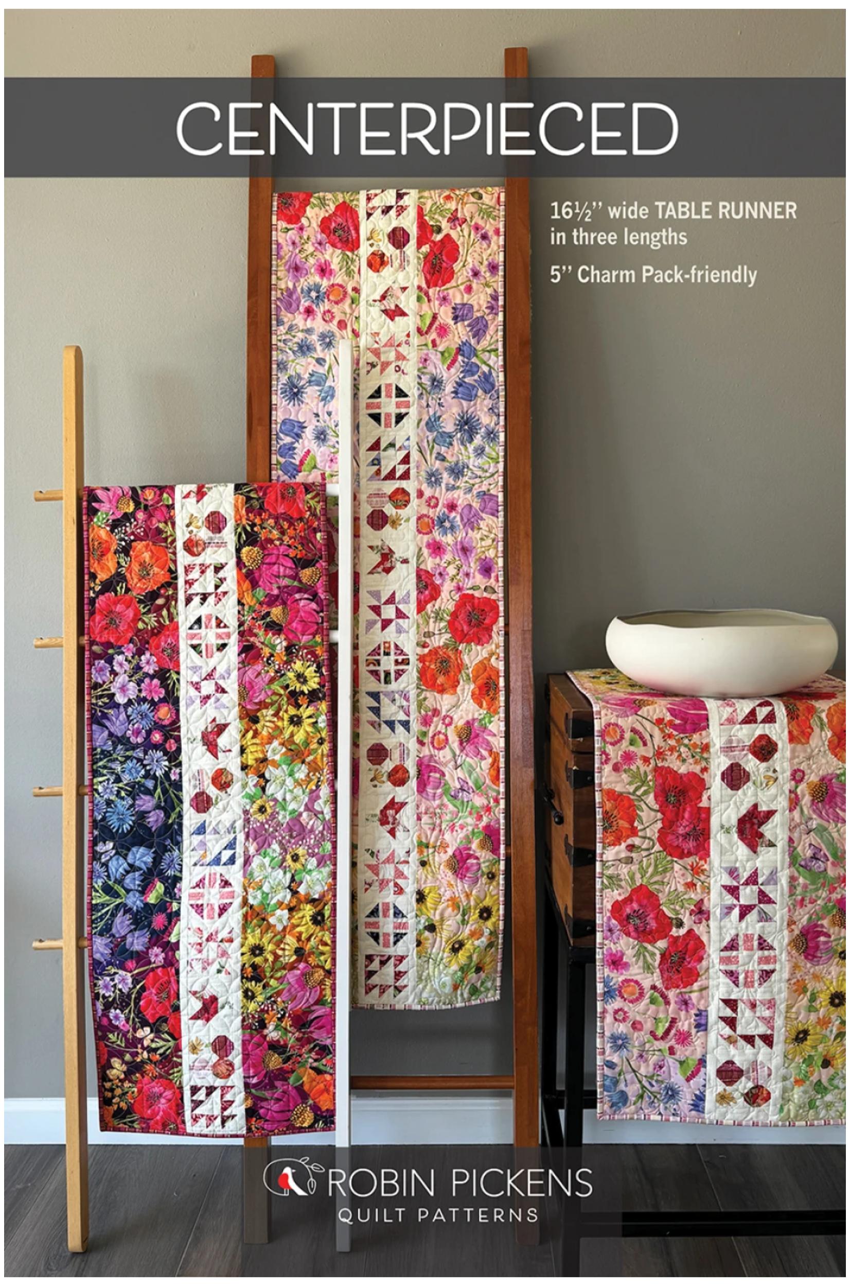 Promotional image for a quilt pattern titled 'CENTERPIECED' by Robin Pickens Quilt Patterns, showing three colorful floral table runners displayed on wooden stands in an indoor room setting.