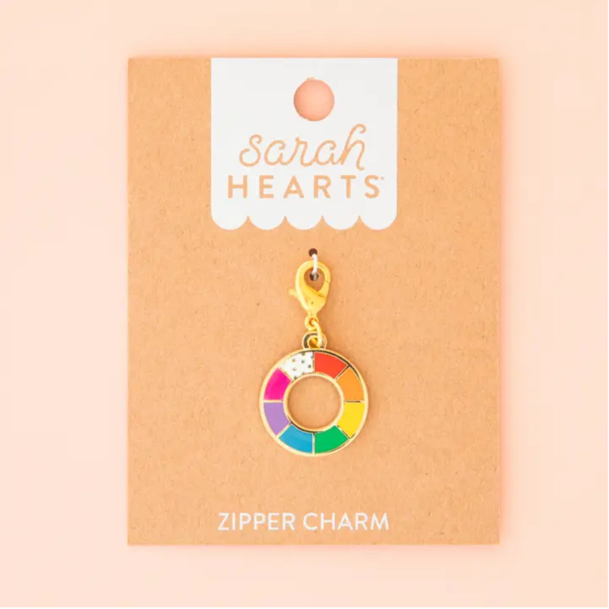 A gold-tone zipper charm shaped like a donut with a rainbow-colored segmented face, displayed on a kraft paper backing card labeled 'Sarah Hearts' and 'ZIPPER CHARM'.