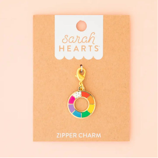 A gold-tone zipper charm shaped like a donut with a rainbow-colored segmented face, displayed on a kraft paper backing card labeled 'Sarah Hearts' and 'ZIPPER CHARM'.