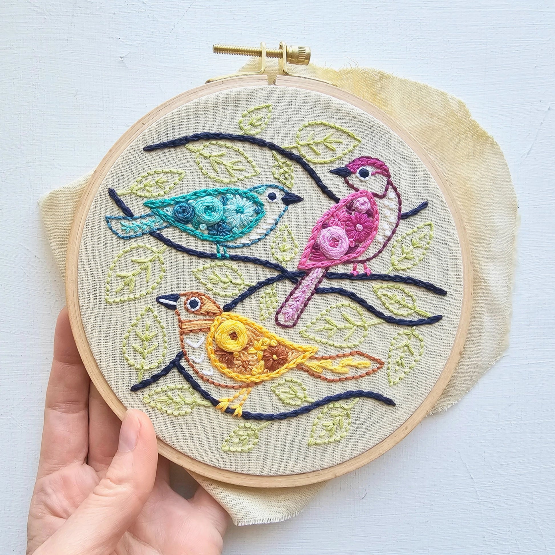 Embroidery hoop with colorful birds and leaves on a white background