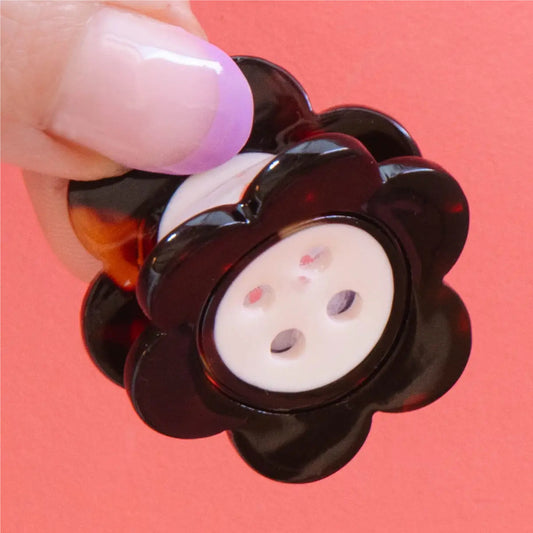 Flower-shaped button with tortoiseshell casing held by a hand against a pink background