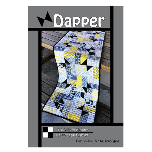 A quilt pattern cover titled 'Dapper' by Tricia Lynn Maleney from Orphan Quilt Designs, for Villa Rosa Designs. The cover features a photo of a geometric patchwork table runner in yellow, gray, black, and white, draped over a wooden table.