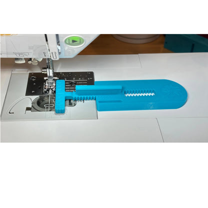 A bright blue plastic sewing machine accessory with a serrated edge and hook-and-loop fastening, shown attached to a white sewing machine.
