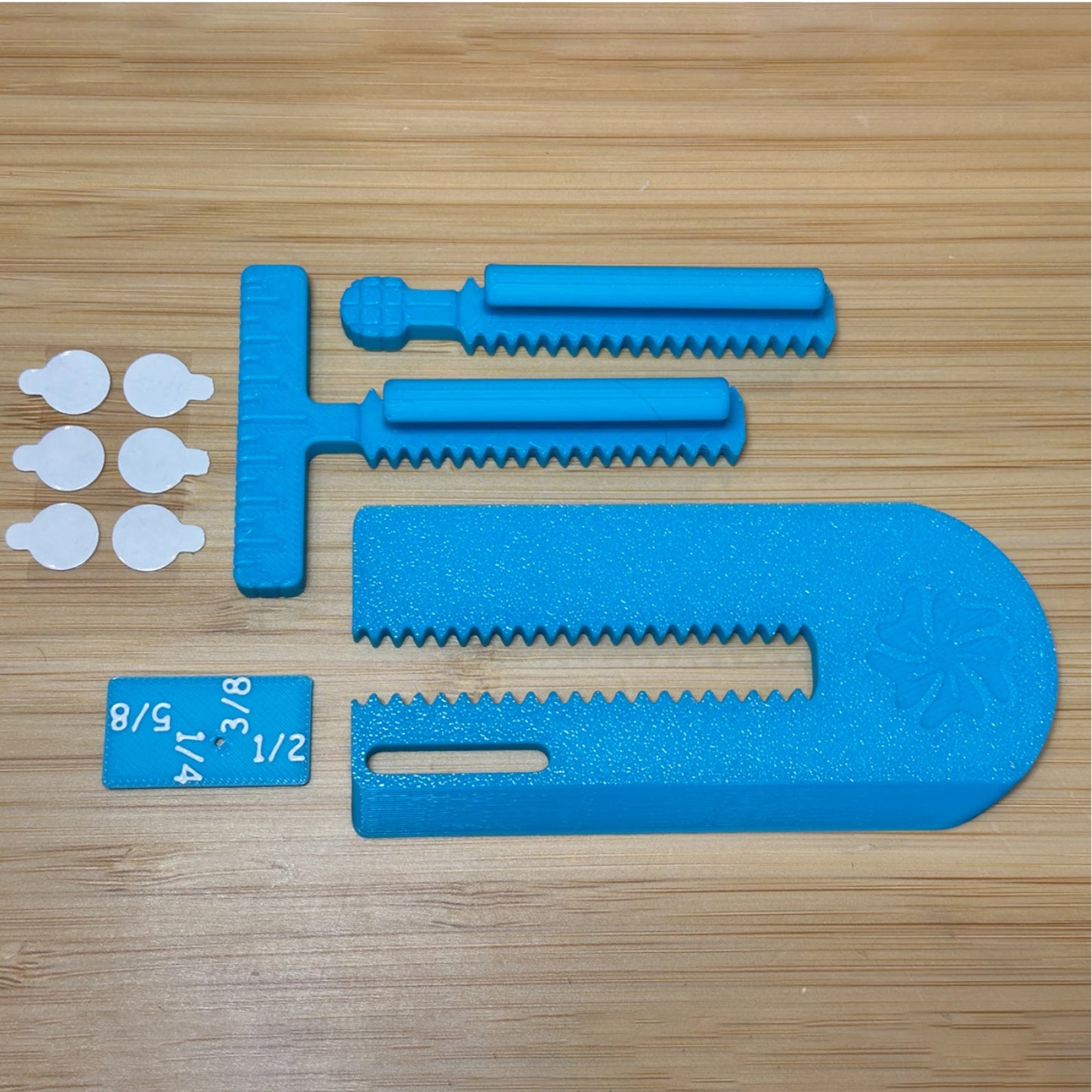Blue plastic tool components laid out on a light wood surface, including a large curved foam piece, two serrated rod pieces, a T-shaped piece, a small blue tag with white size markings, and six small white circular pieces.