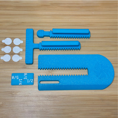 Blue plastic tool components laid out on a light wood surface, including a large curved foam piece, two serrated rod pieces, a T-shaped piece, a small blue tag with white size markings, and six small white circular pieces.