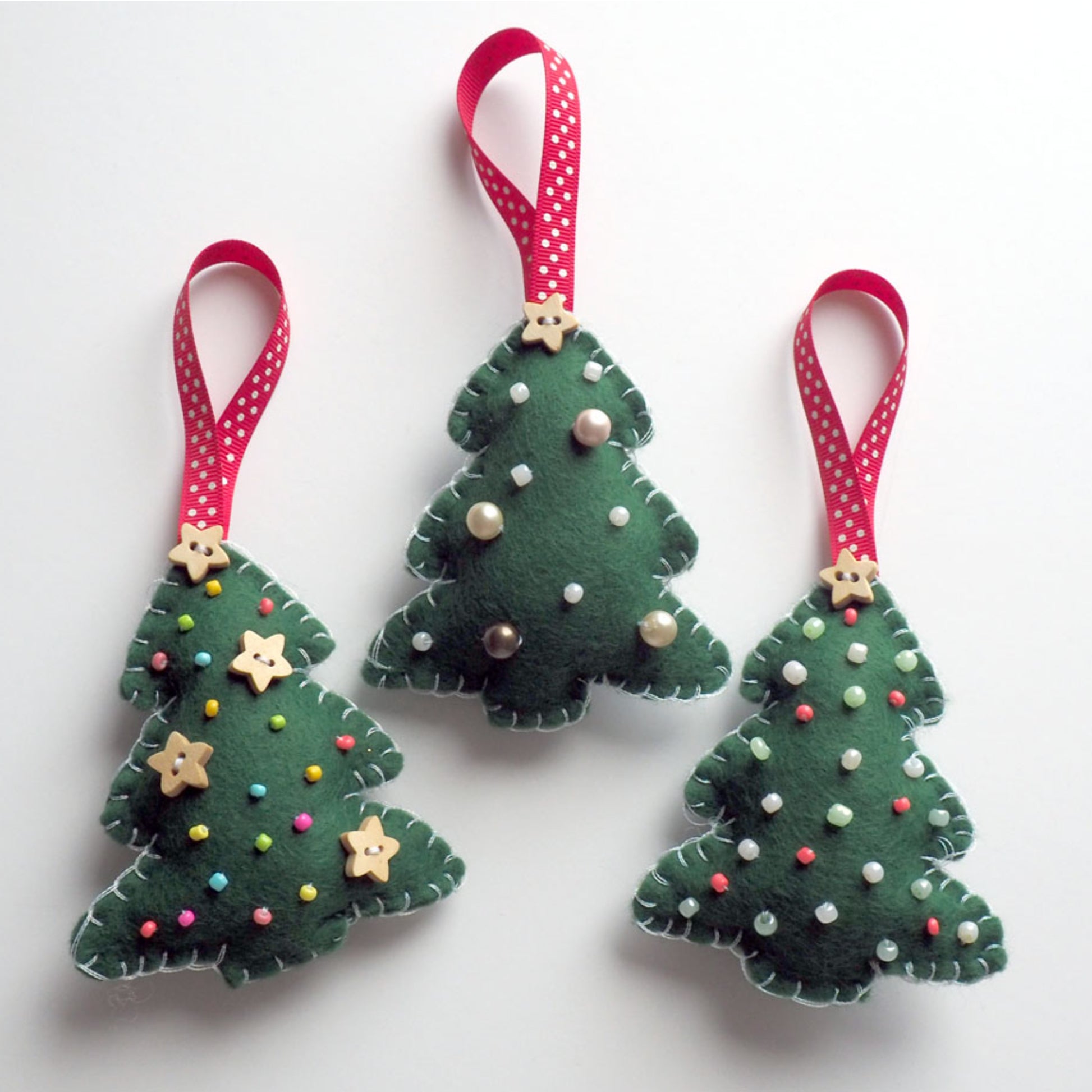 Three green felt Christmas tree ornaments with red ribbons on a white background