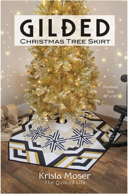A quilted Christmas tree skirt with a geometric black, white, and gold pattern, shown under a gold tinsel Christmas tree. The image features text overlays reading 'GILDED CHRISTMAS TREE SKIRT' and 'Krista Moser The Quilted Life'.