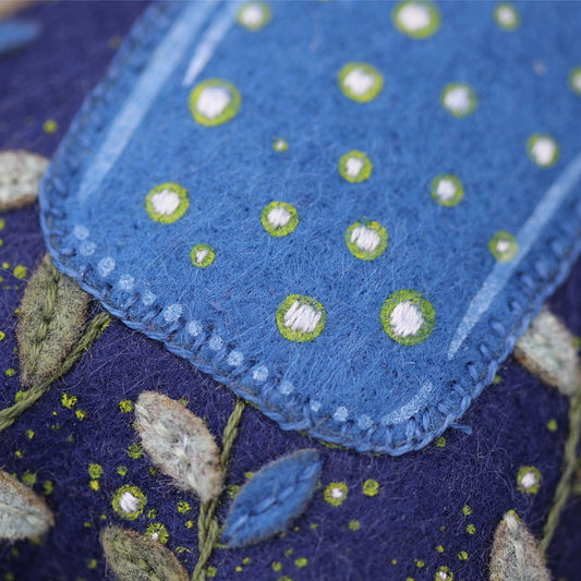 Blue embroidered fabric with green and white patterns on a dark background