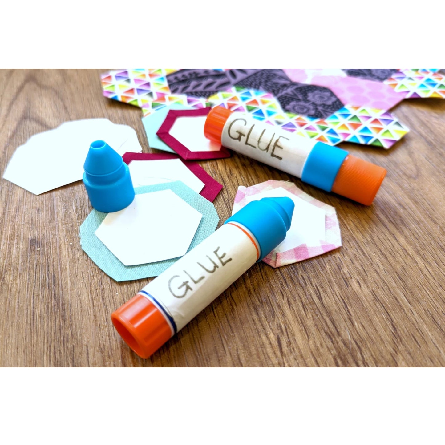 Two glue sticks with colorful shapes on a wooden surface