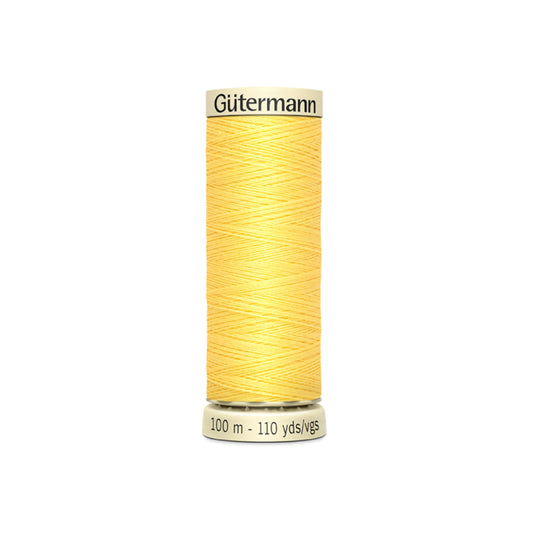 Spool of yellow Gutermann thread on a white background