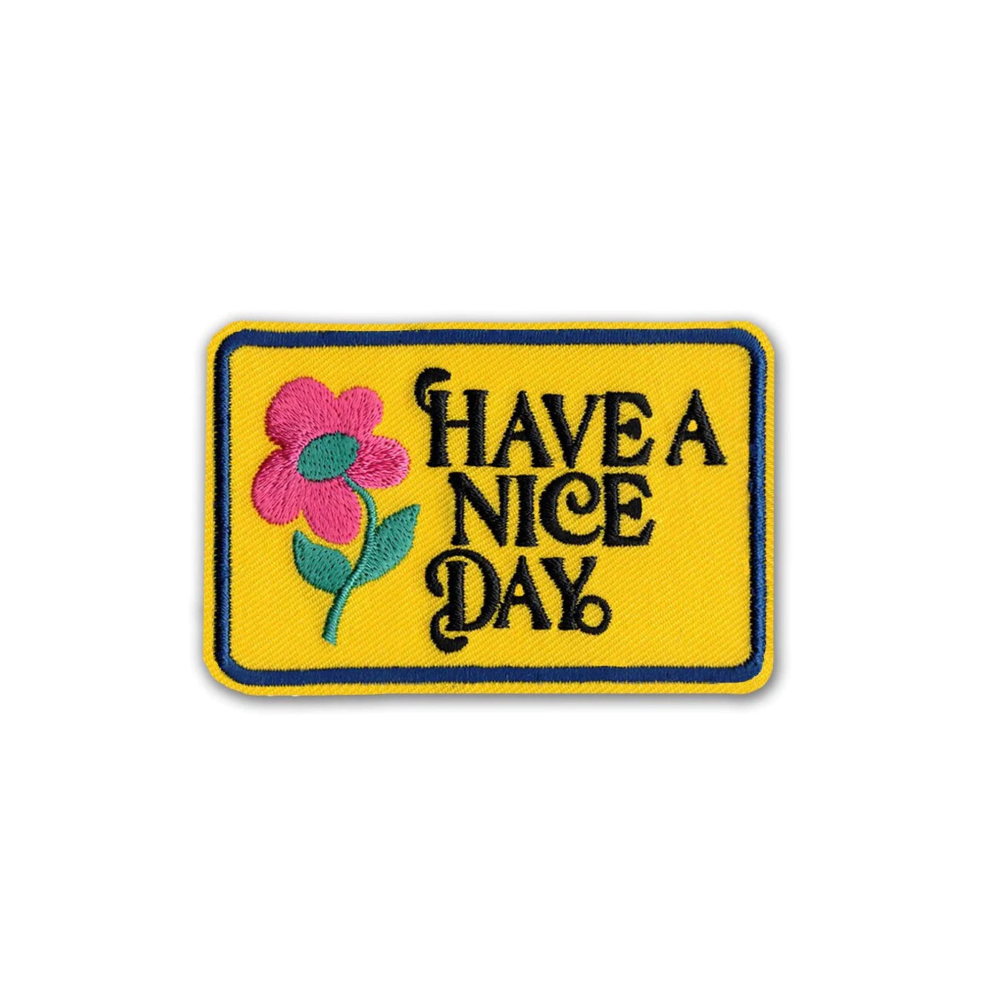 A rectangular embroidered patch with a yellow background, a pink flower with green leaves on the left, and the phrase 'HAVE A NICE DAY' in black stylized lettering, shown on a plain white background.