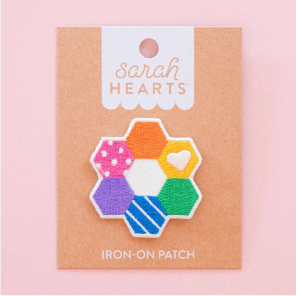 A colorful embroidered iron-on patch shaped like a honeycomb, displayed on a kraft paper backing card with the brand name 'Sarah Hearts' printed at the top. The patch features multiple colored sections with different embroidery patterns, including polka dots, stripes, and a white heart.