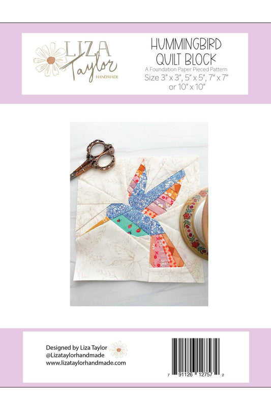Back cover of a quilting pattern package for the Hummingbird Quilt Block by Liza Taylor, showing a fabric hummingbird patch on a quilted square, with scissors and fabric roll nearby. The package has a white and pale lavender design with product title, sizes, and a barcode.
