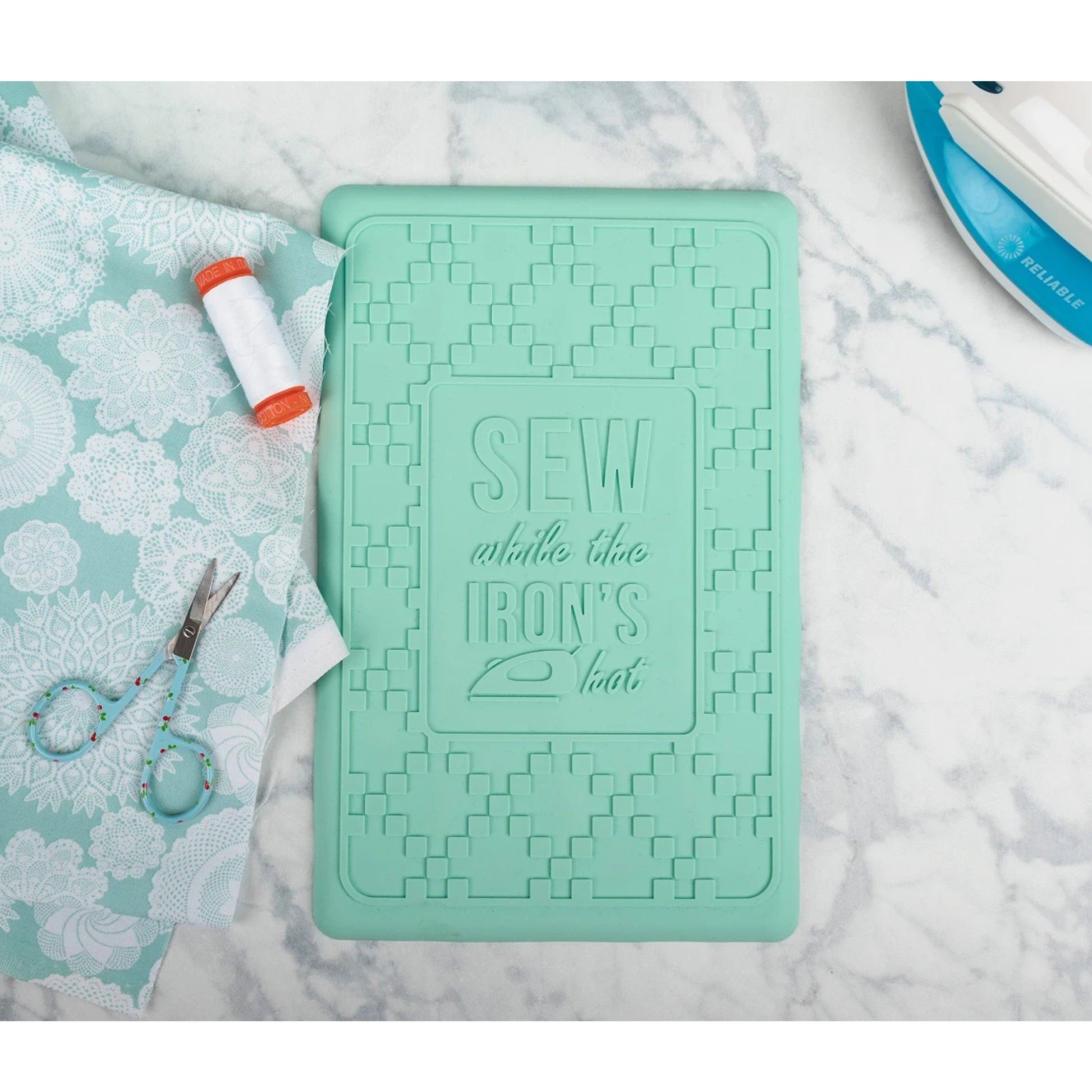 Mint green iron rest with text on a marble surface with sewing tools.
