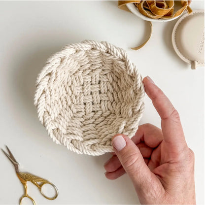 Hand holding a woven beige bowl with scissors and other items in the background