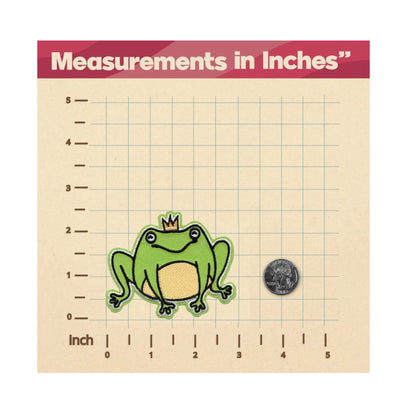 A square measurement card showing a green cartoon frog wearing a small gold crown and a quarter for scale, with inch grid lines and the text 'Measurements in Inches' at the top.
