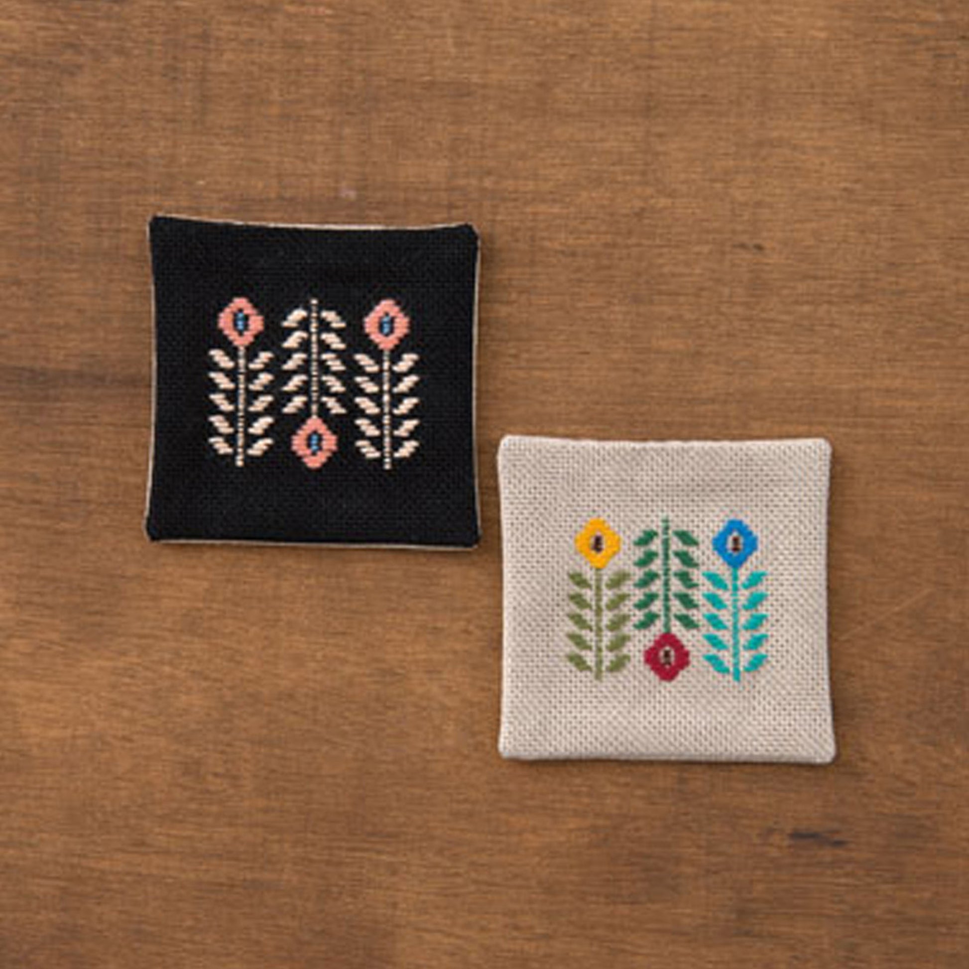 Two embroidered square coasters on a wooden surface