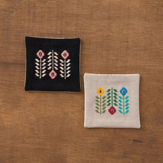 Two embroidered square coasters on a wooden surface