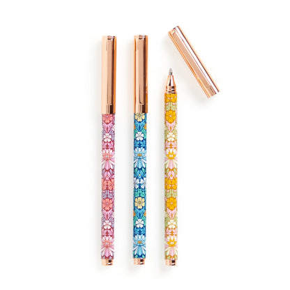 Three floral patterned gel pens with rose gold metal accents and a matching cap, arranged on a clean white background.