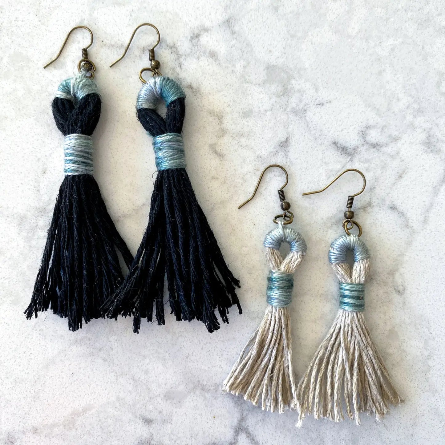 Pair of black tassel earrings and a pair of silver tassel earrings on a marble surface.