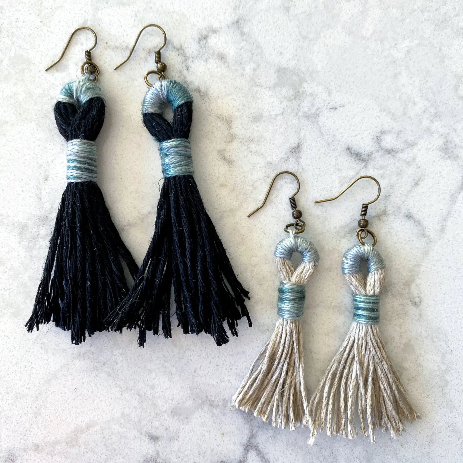 Pair of black tassel earrings and a pair of silver tassel earrings on a marble surface.