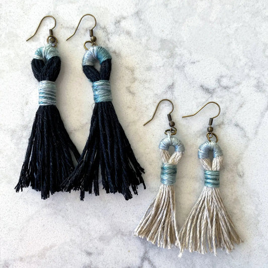 Pair of black tassel earrings and a pair of silver tassel earrings on a marble surface.