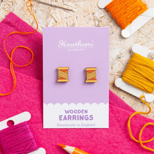 Wooden earrings on a purple card with yarn and knitting tools in the background