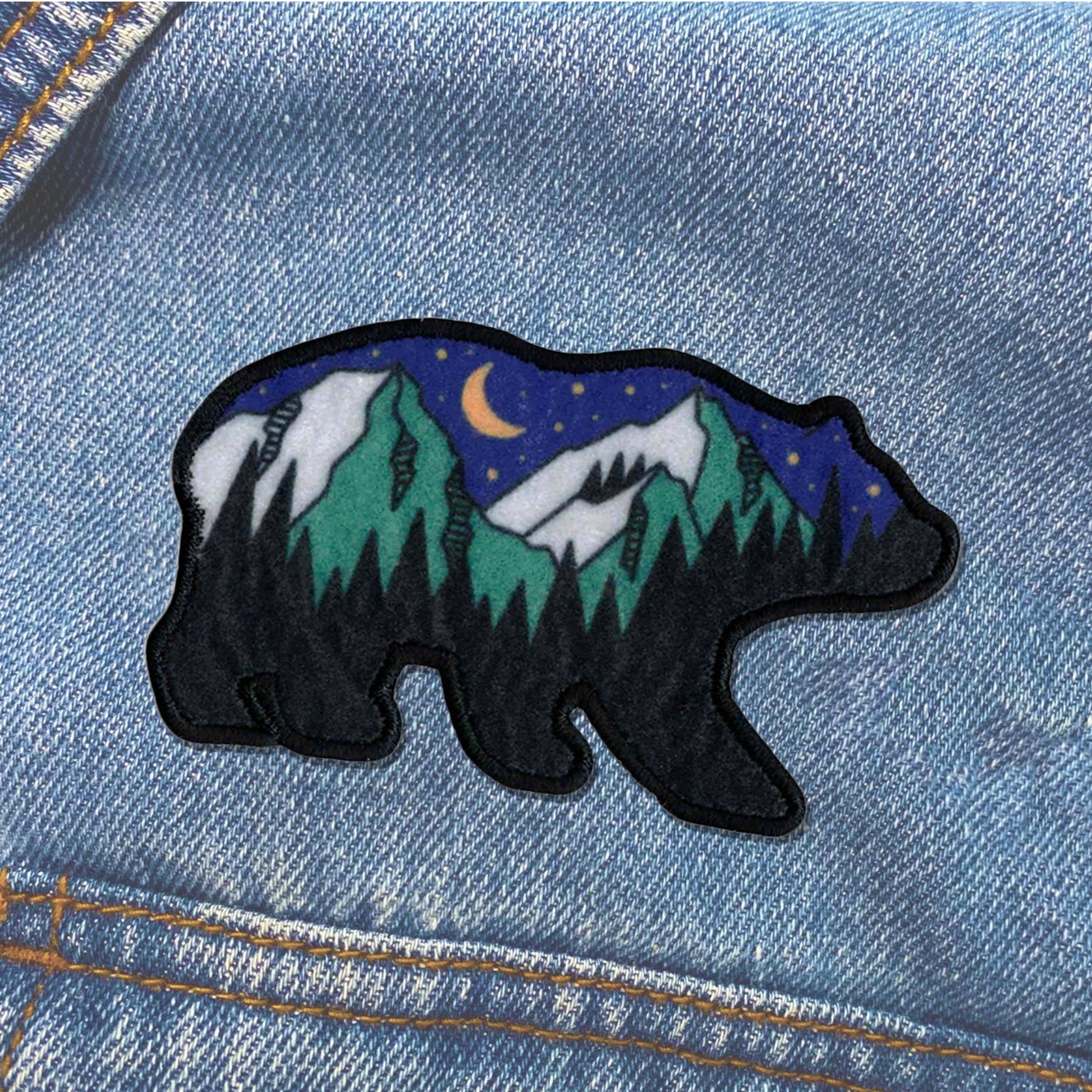 Embroidered bear patch with mountain and moon design on denim fabric