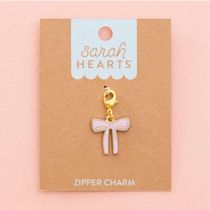A pink bow-shaped zipper charm with a gold clasp, displayed on a brown kraft card labeled 'Sarah Hearts' against a soft pink background.