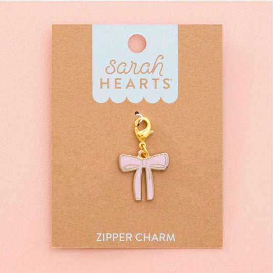 A pink bow-shaped zipper charm with a gold clasp, displayed on a brown kraft card labeled 'Sarah Hearts' against a soft pink background.