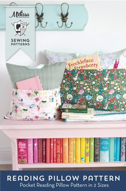 A sewing pattern promotional image for Melissa's Sewing Patterns featuring 'Reading Pillow Pattern' in two sizes. The scene shows several colorful, patterned reading pillows arranged on a pink bench with a row of books underneath, a light blue wall with hooks above, and a banner for Melissa's Sewing Patterns.