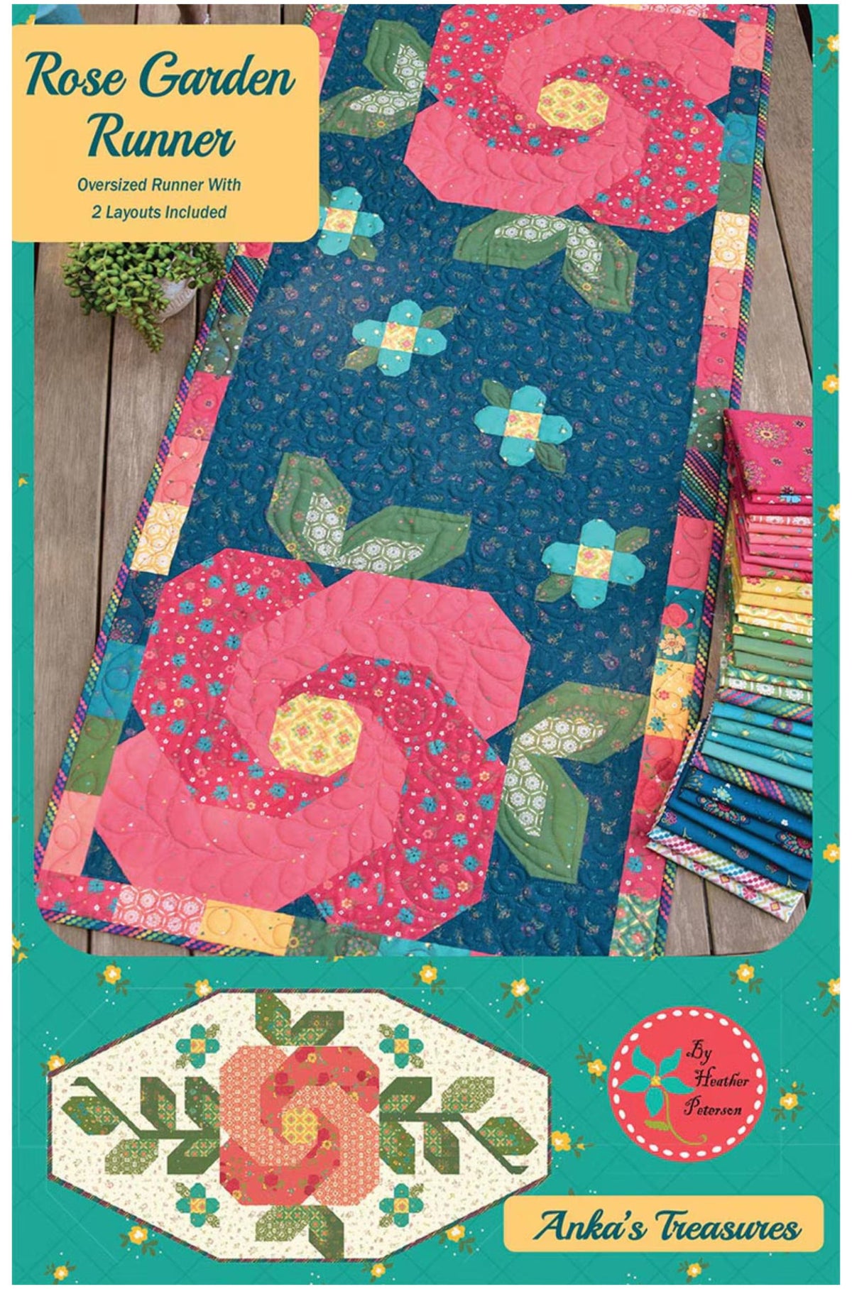 A quilted fabric runner titled 'Rose Garden Runner' shown laid flat on a wooden surface, with a stack of matching fabric pieces and a small plant beside it. The design features large pink roses, green leaves, and blue floral motifs on a dark blue background.