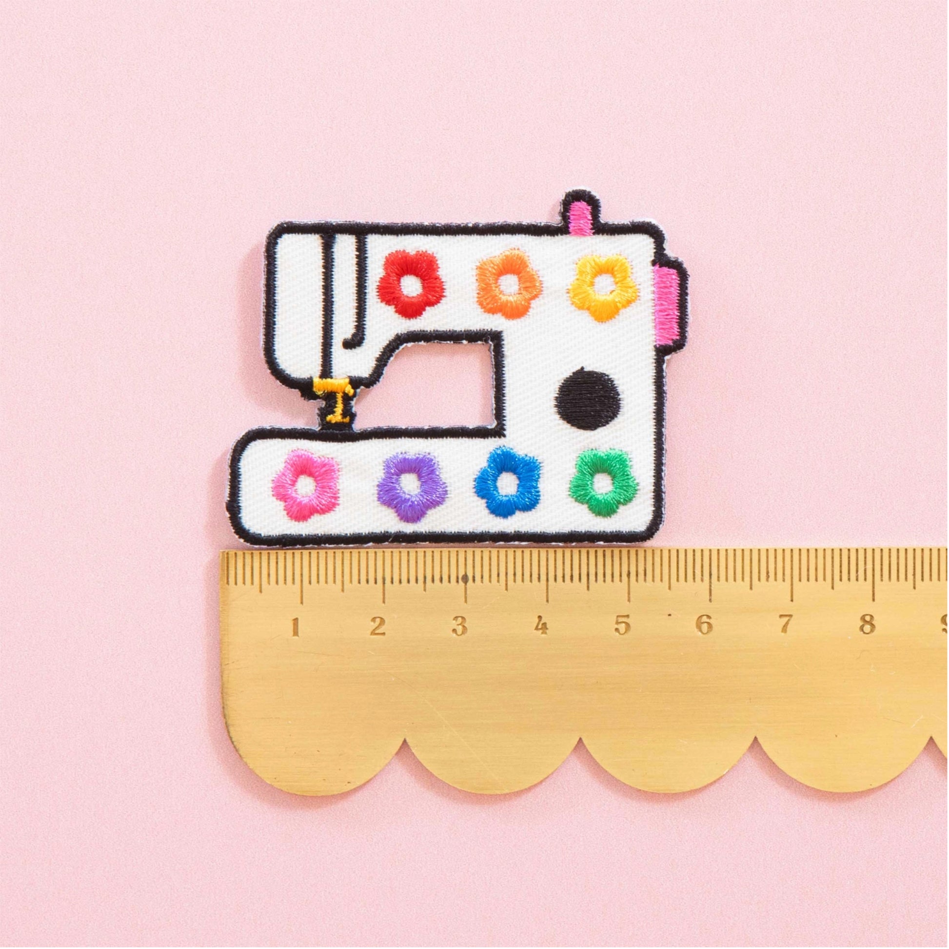 Embroidered patch of a sewing machine with colorful flowers on a pink background