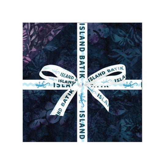 A square fabric bundle wrapped in dark navy batik-patterned paper and tied with a white ribbon printed with 'ISLAND BATIK' and small blue motifs, shown on a white background.