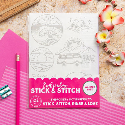 Embroidery Stick & Stitch kit featuring 11 embroidery motifs on a white sheet, styled in a flat-lay with a pink pencil, pink paper, and flowers on a textured beige background.